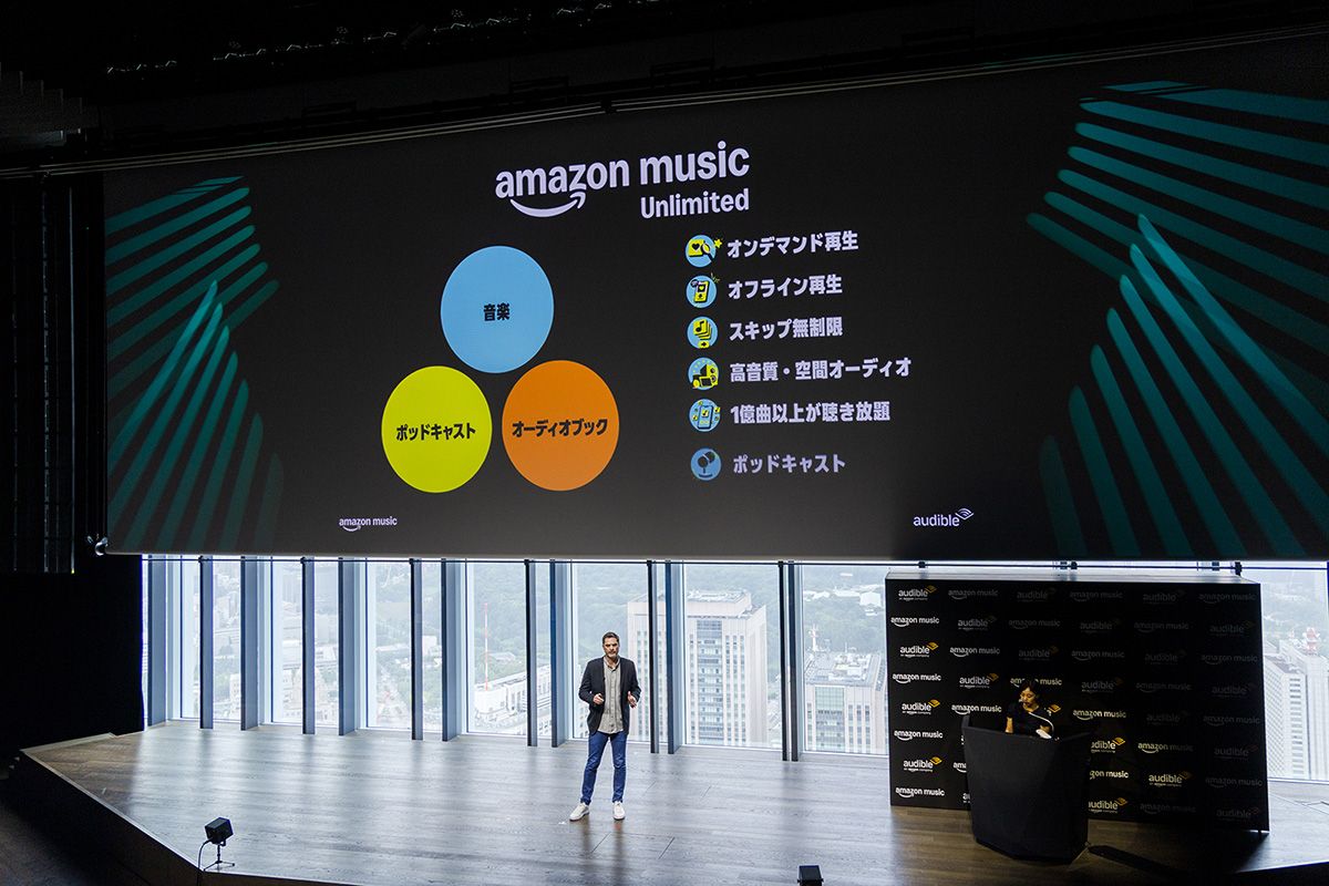  発表会のステージで月額1080円で提供されているAmazon Music Unlimitedの特徴を語るライアン氏。1億曲を超える音楽作品とポッドキャストのほか、Audibleのオーディオブックが楽しめるようになった