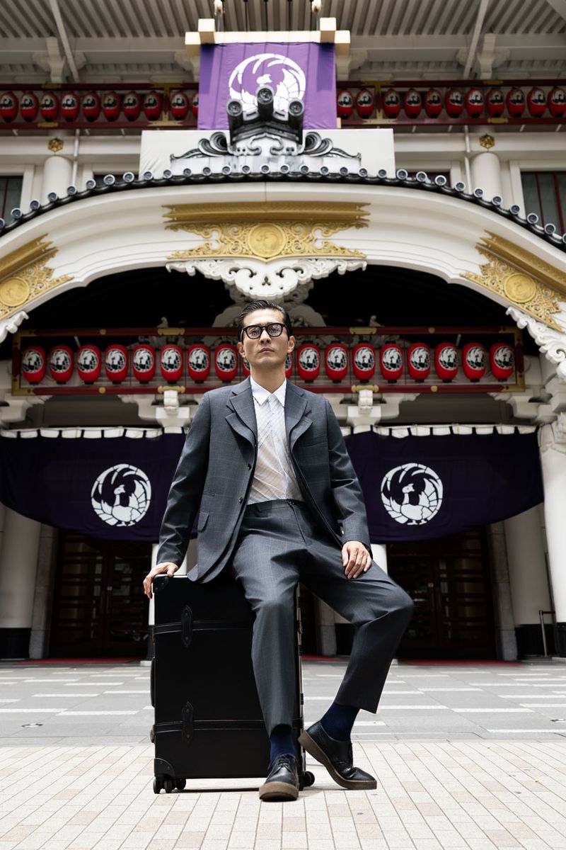 ジャケット209000円、パンツ90200円、シャツ34100円、靴96800円〈すべてコム デ ギャルソン・オム ドゥ／コム デ ギャルソン Tel:03-3486-7611〉メガネ49500円〈モスコット／モスコット トウキョウ Tel:03-6434-1070〉トロリーケース451000円〈グローブ・トロッター／グローブ・トロッター銀座 Tel:03-6161-1897〉※ソックスはスタイリスト私物。