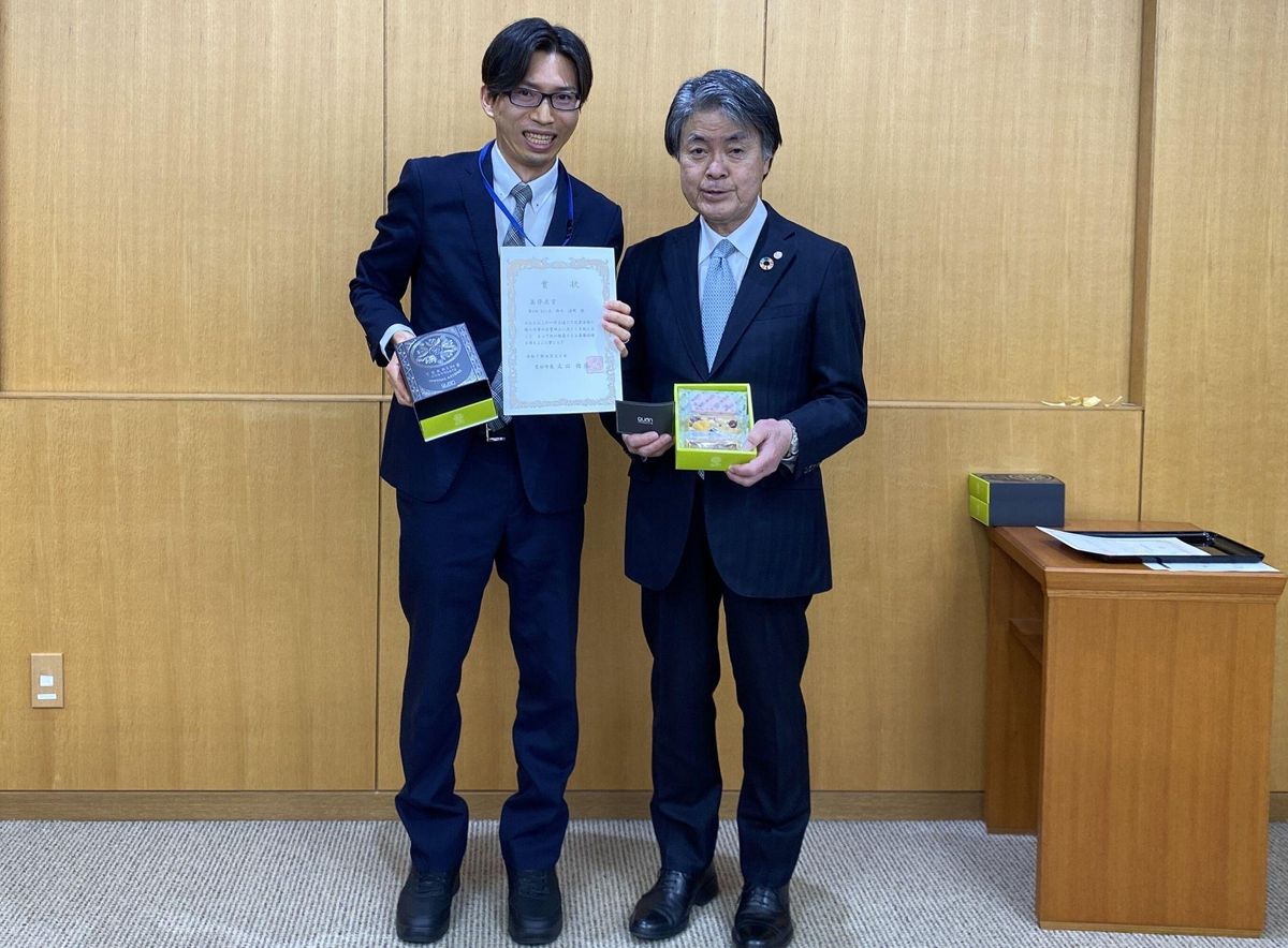 謙虚で愚直 若き改善の求道者 鈴木満明(左) 。役所内の改善提案制度で高得点賞を獲得し市長から表彰される。NECソリューションイノベータ賞とのW受賞