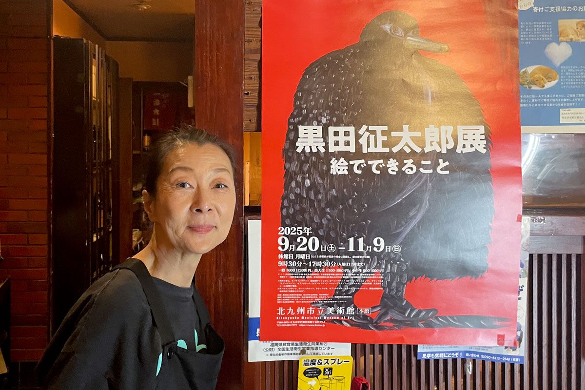 一番太鼓の女将じゅんさん。黒田征太郎展のポスターとともに