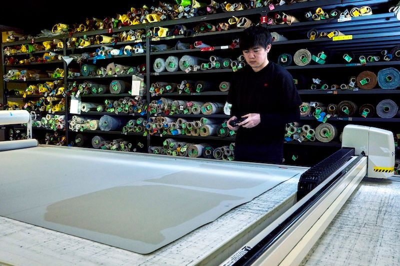 牛革の型の切り抜きは機械で自動化されているため、複雑な曲線も自由自在。コントローラーで遠隔操作する。革の検品にも余念がない。