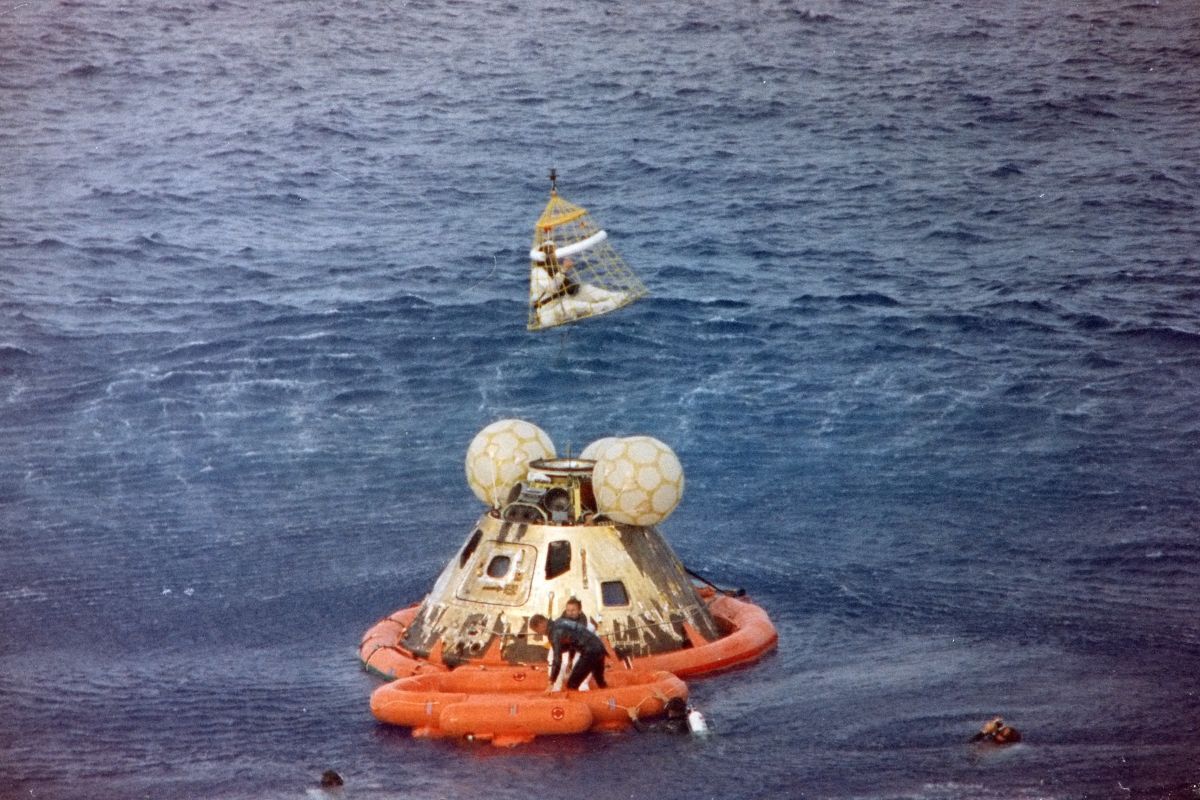 NASAの「アポロ13号」ミッションで地球に帰還した乗組員たちの回収任務の様子。司令船操縦士のジョン・スワイガート宇宙飛行士がヘリに引き上げられる間、船長のジェームズ・ラベル宇宙飛行士は救命ボートで潜水士と待機しており、海面にも潜水士の姿が見える。1970年4月17日撮影(NASA, Public domain, via Wikimedia Commons)